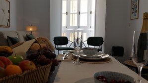 Uma sala de jantar com uma mesa posta para dois, uma cesta de frutas e uma garrafa de champanhe.