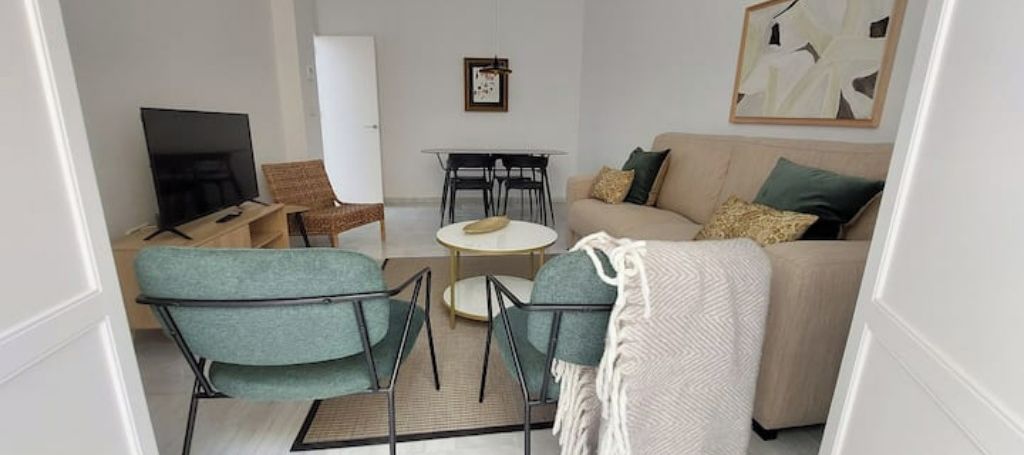 A living room with a sofa, two armchairs, a coffee table, a TV, and a dining table with chairs.