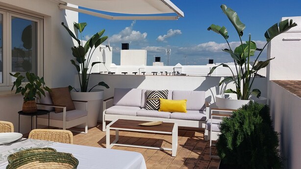 A sunlit patio with a dining table, chairs, a sofa, and potted plants. - 2 Flamenco AticoB (Cádiz)