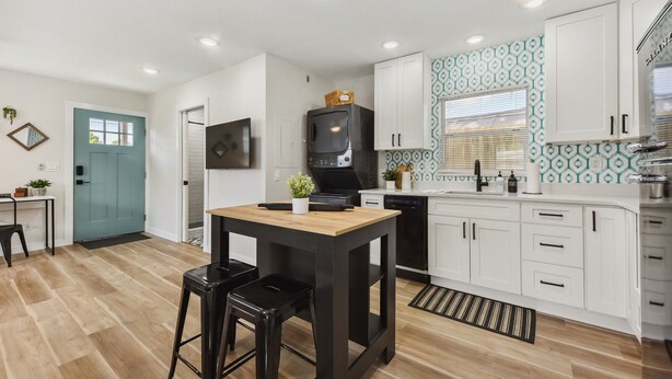 A modern kitchen with white cabinets, a black countertop, and a wooden dining table with two stools. - Quiet Studio Guesthouse in Jax - Near Downtown (Jacksonville)