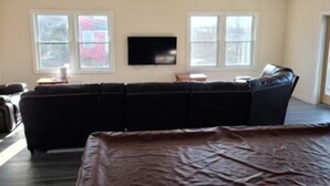 Un salon doté d’un canapé d’angle, d’un téléviseur à écran plat fixé au mur et de grandes fenêtres laissant entrer la lumière naturelle.
