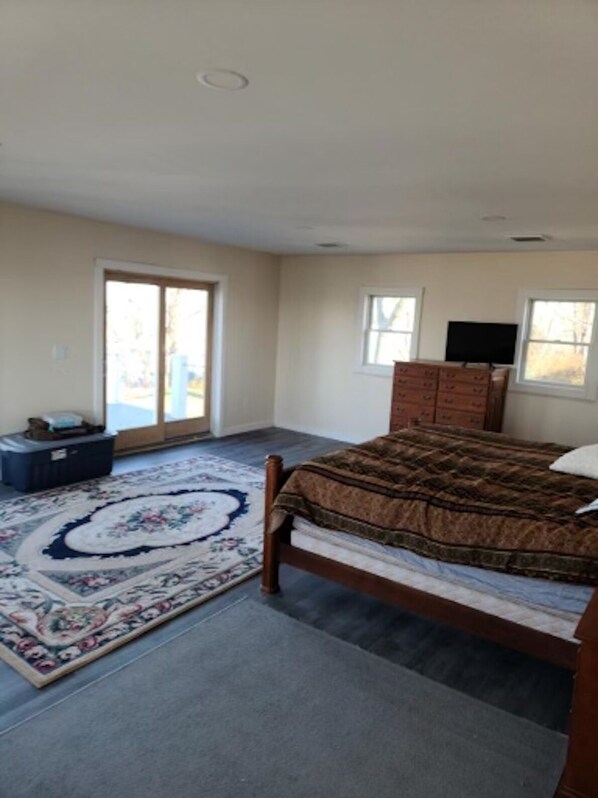 A bedroom with a bed, a dresser, a television, and a large window. - Skyline Views (Nahant)