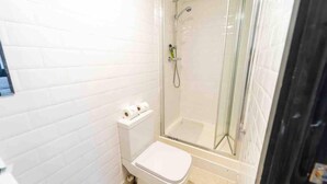 A small bathroom with a toilet, a shower, and a glass-enclosed shower area. - Ground Floor Cosy Studio Close to the City (Birmingham)