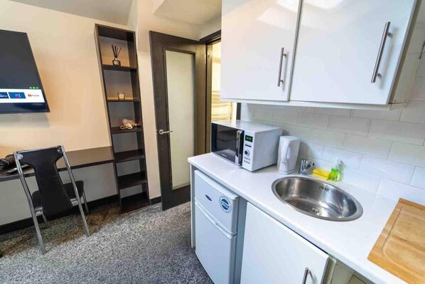 A compact kitchen with white cabinets, a microwave, a sink, and a small countertop.