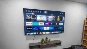 Un téléviseur à écran plat fixé au mur, avec une étagère en dessous sur laquelle sont affichés divers logos de services de diffusion en continu.