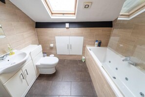A bathroom with a skylight, a toilet, a sink, a bathtub, and cabinets.