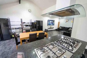 Una cocina moderna con estufa a gas, una mesa de comedor, sillas, un refrigerador y un televisor en la pared.