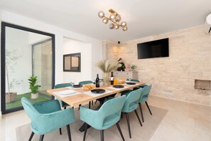 Un coin repas avec une table en bois, des chaises de couleur turquoise et un mur en pierre agrémenté d’un téléviseur.
