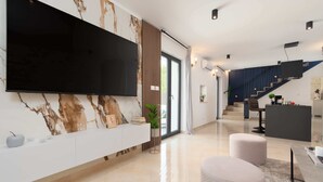 Ein modernes Wohnzimmer mit großem Flachbildfernseher, Marmorwand, Treppe und Essbereich.