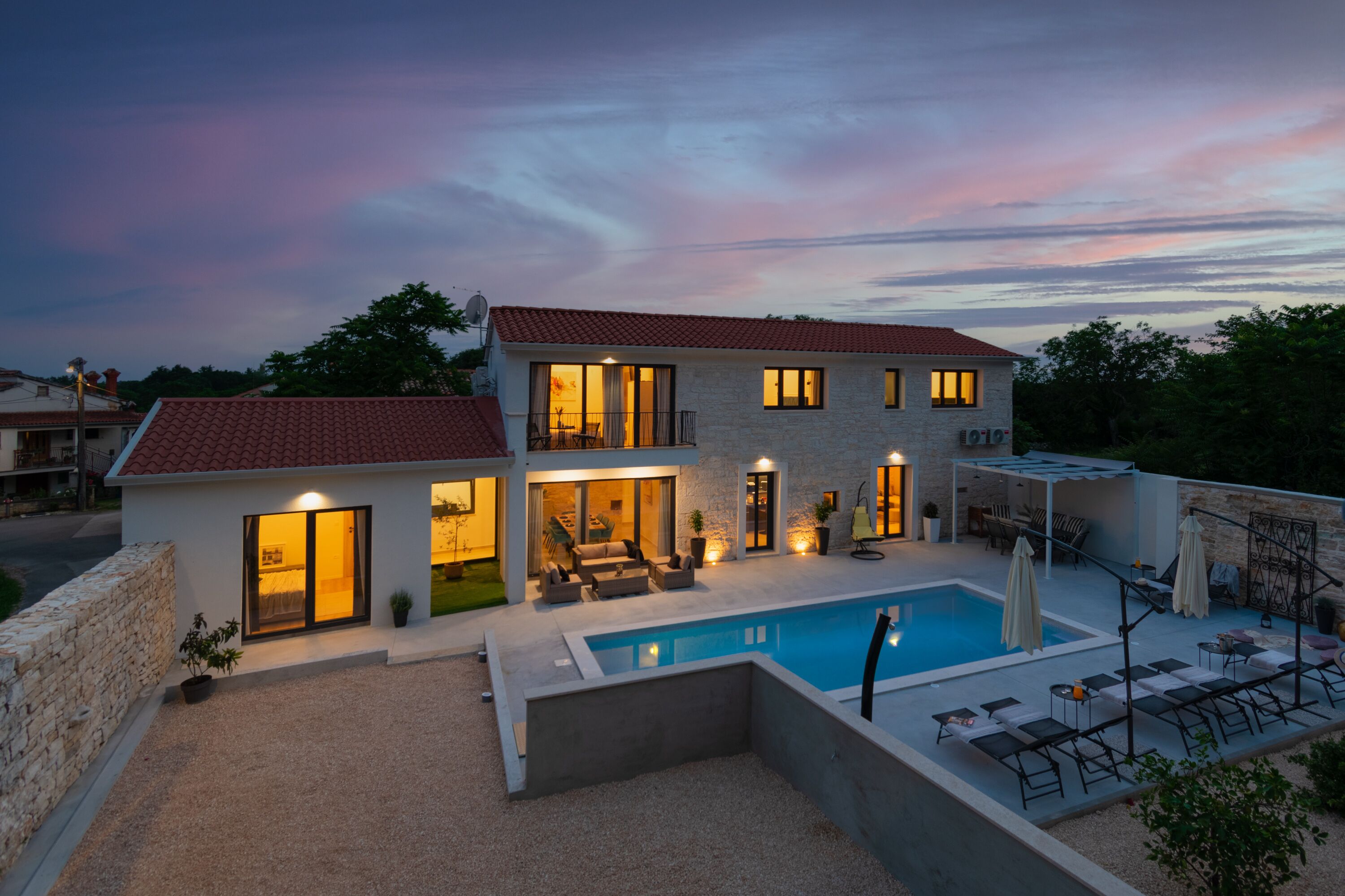 A two-story house with a swimming pool, outdoor seating, and a stone wall.