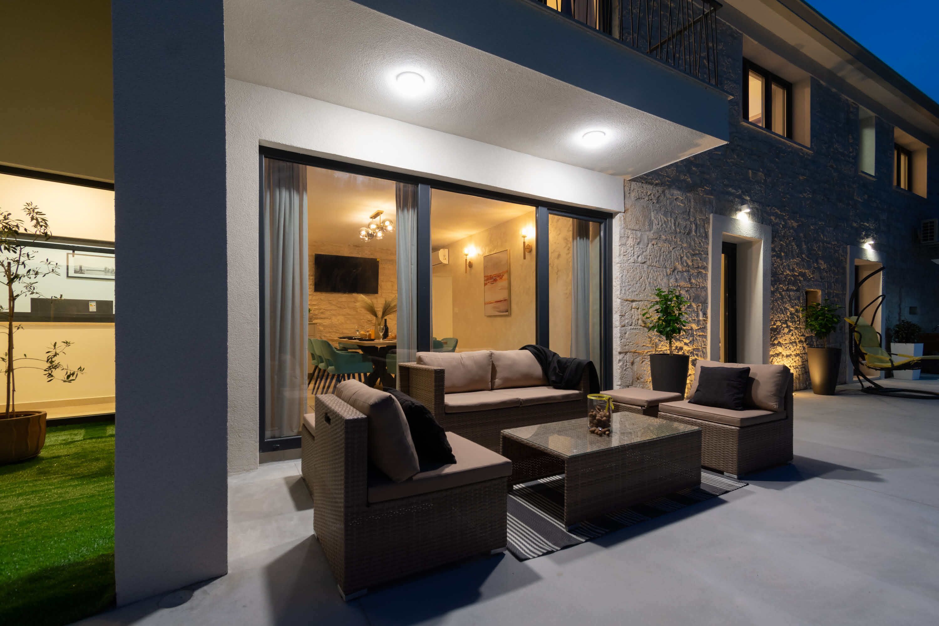 Un espace extérieur aménagé avec des meubles en osier et une table basse en verre, offrant une vue sur un espace intérieur bien éclairé, comprenant un coin repas.