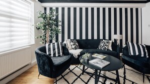 A modern living room with a black and white striped wall, a dark blue sofa set, a round coffee table, and a large plant. - Chic 1 Bed Flat Zone 2 Hampstead Swiss Cottage (London)