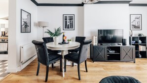 A modern living room with a dining area, featuring a round table, black upholstered chairs, a flat-screen TV, and a bookshelf. - Chic 1 Bed Flat Zone 2 Hampstead Swiss Cottage (London)