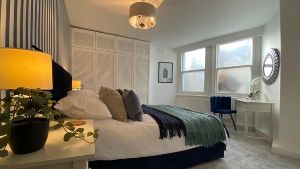 A bedroom with a bed, bedside table, lamp, potted plant, and a desk with a chair. - Chic 1 Bed Flat Zone 2 Hampstead Swiss Cottage (London)