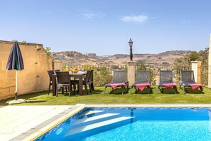 A swimming pool with lounge chairs and a table with chairs, surrounded by a stone wall and a view of hills. - Ta Lucija Sleeps 4 With Private Pool (Xaghra)