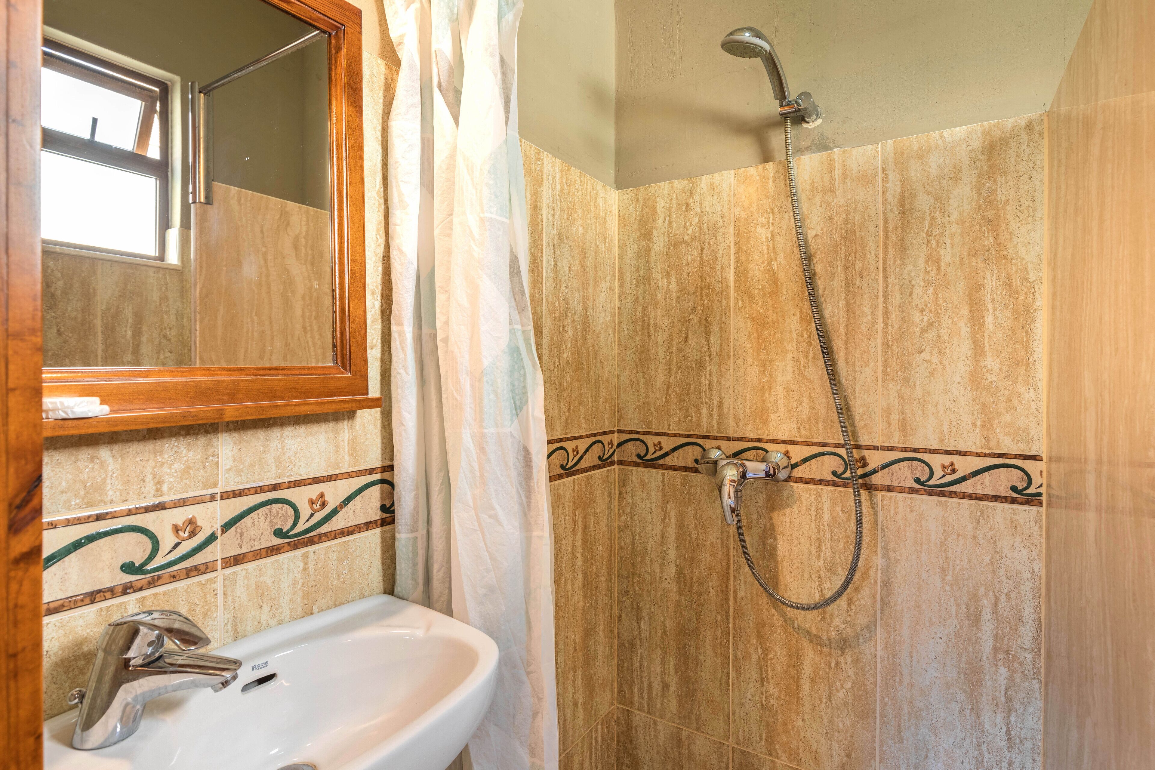 A bathroom with a sink, mirror, shower, and decorative tile border.