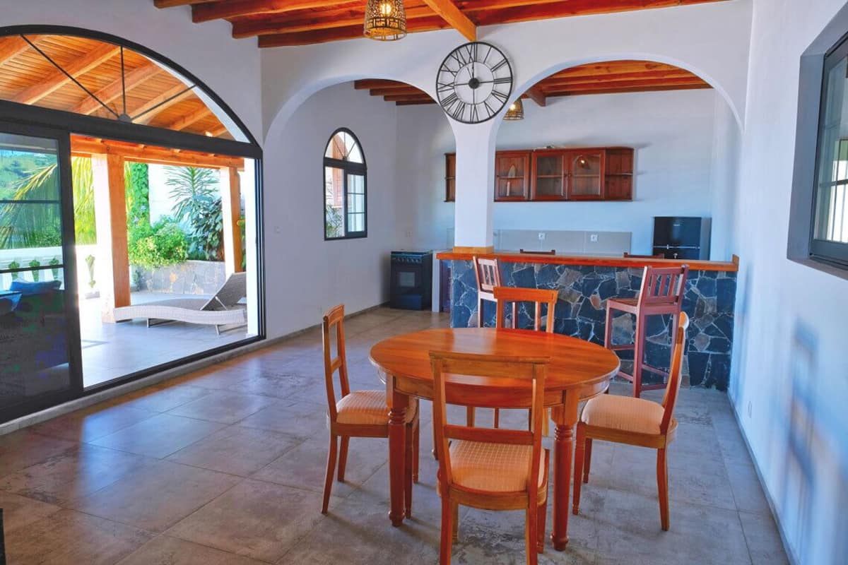 Un comedor con una mesa y sillas de madera, una pared de acento de piedra y una cocina con armarios de madera y un reloj.
