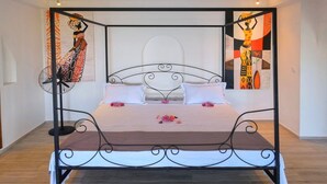 A four-poster bed with a white bedspread and pink flowers, set in a room with wooden flooring and two abstract paintings on the walls. - Les Terrasses d'Ulysse (Nosy Be)