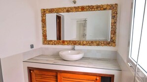 A bathroom with a stone-framed mirror, a white sink, and wooden cabinets. - Les Terrasses d'Ulysse (Nosy Be)