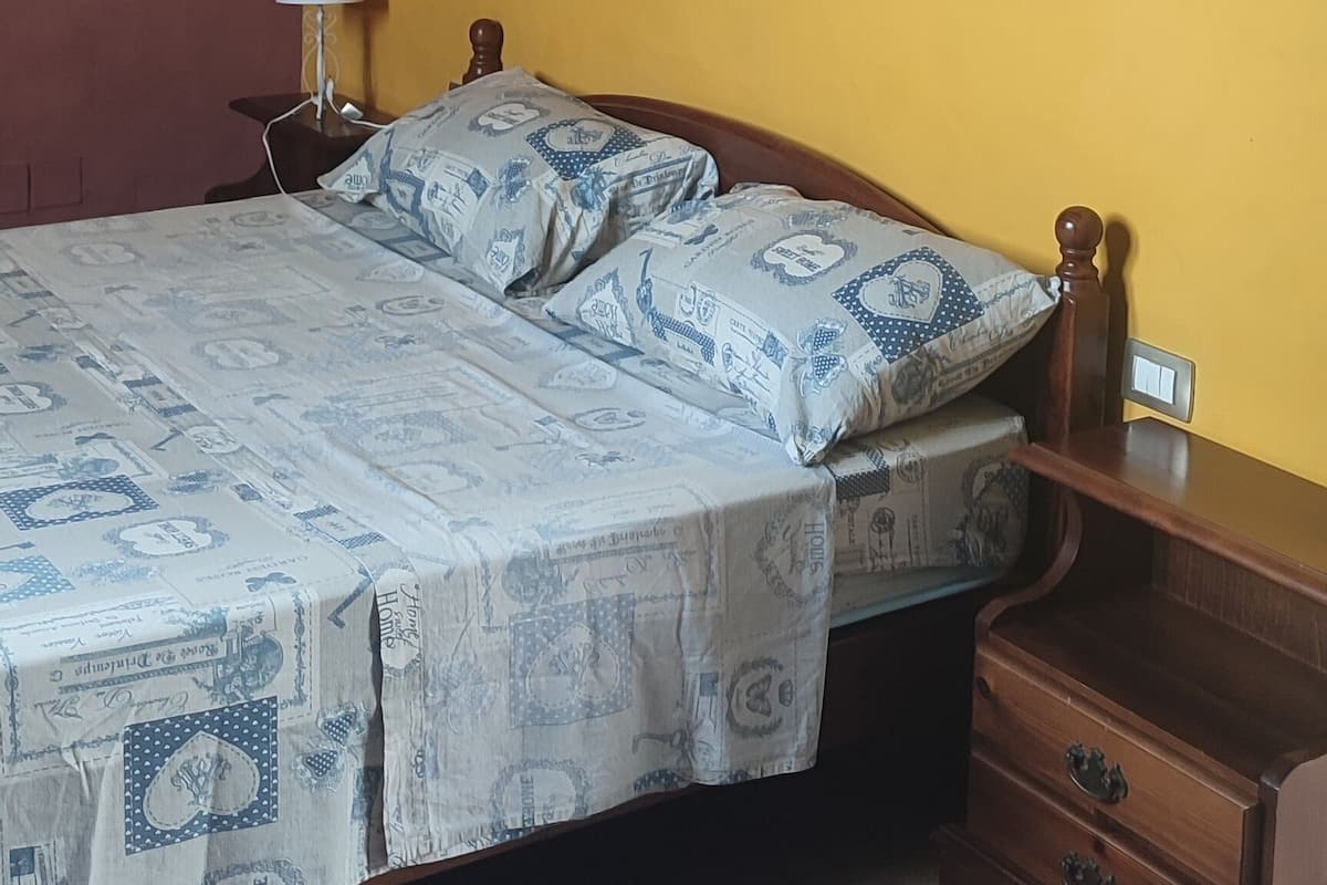 A bedroom with a bed, nightstand, lamp, and a wooden dresser.
