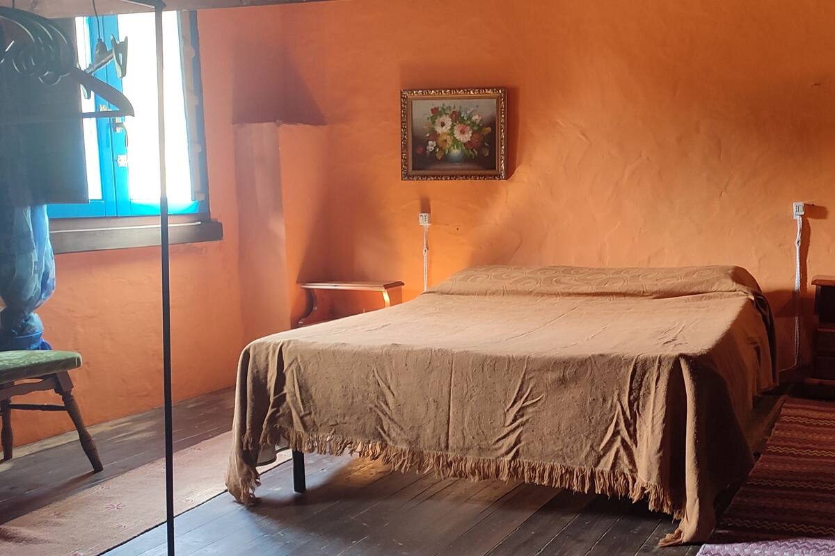 A room with a bed, a nightstand, a lamp, a window, and a painting on the wall.