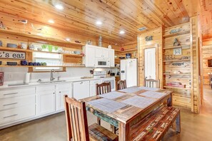Una cocina estilo cabaña de madera con armarios blancos, una mesa de comedor con bancos y un cartel que dice 'Beach'.