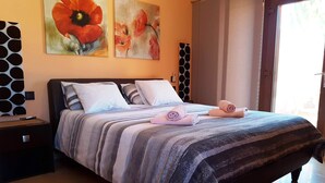 A neatly made bed with striped bedding, two pillows, and rolled towels. There are two paintings on the wall, a window with curtains, and a patterned wall decoration. - Exclusive Finca with Pool – Away from Mass Tourism – Peaceful Location! (Triquivijate/Antigua)