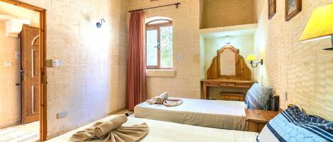 A room with two beds, a wooden door, a window with a curtain, a wooden cabinet, and a wall-mounted lamp.