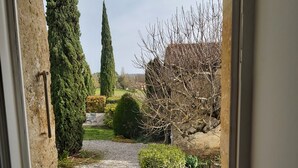 A view through a window of a garden with a gravel path, various shrubs, and a tall tree. - "Nouveau, a true haven of peace, close to Saint-Emilion, Bordeaux. (Saint-Vincent-de-Pertignas)