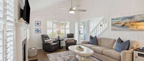 A living room with a fireplace, a ceiling fan, a sofa with cushions, and a painting on the wall.