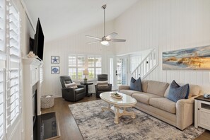 Ein Wohnzimmer mit Kamin, Deckenventilator, einer Couch mit Kissen und einem Bild an der Wand.