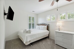 A bedroom with a bed, a nightstand, a wall-mounted TV, and a ceiling fan.