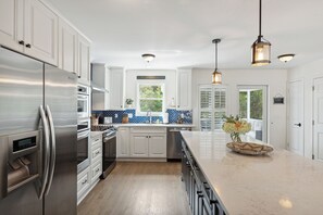 A modern kitchen with white cabinetry, stainless steel appliances, and a marble countertop.