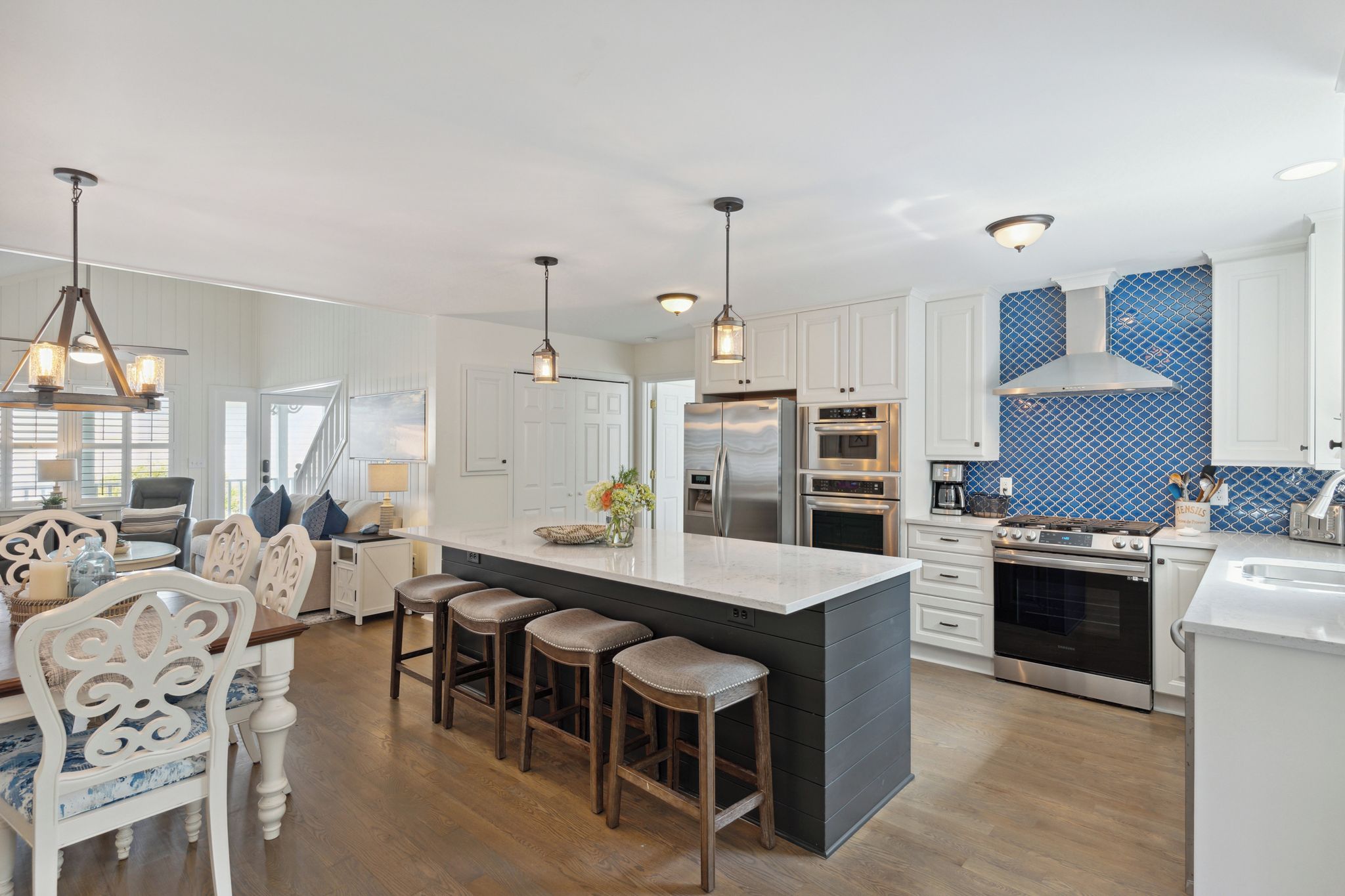 A modern kitchen with a central island, bar stools, stainless steel appliances, and pendant lighting.