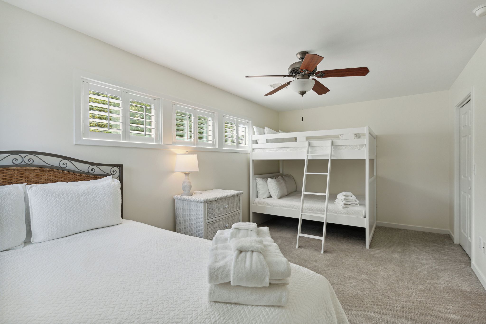 A bedroom with a bunk bed, a single bed, a nightstand, a lamp, and a ceiling fan.