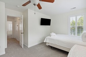 Ein Schlafzimmer mit einem Bett, einem Deckenventilator, einem Fernseher und einem Fenster mit Jalousien.