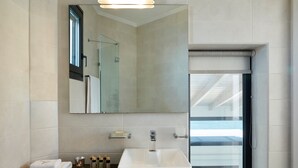 A modern bathroom with a large mirror, a white sink, and a window providing a view of the outdoors. - Eleia Seafront VIlla with Private Pool & Sea View (Lesvos)