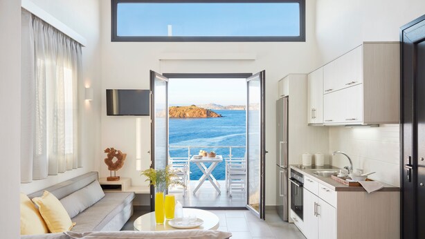 A modern kitchen with a view of the sea, a dining area with a table and chairs, and a sofa with cushions. - Eleia Seafront VIlla with Private Pool & Sea View (Lesvos)