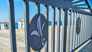 A metal fence with decorative circular elements and a view of a beach and buildings in the background. - Eleia Seafront VIlla with Private Pool & Sea View (Lesvos)