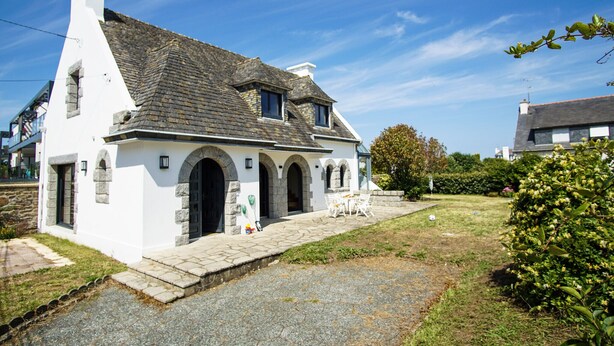 Un bâtiment blanc avec une façade en pierre, un toit recouvert de tuiles et une entrée pavée.