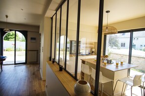A modern kitchen with a large window, wooden flooring, and a dining area with white chairs. - -TY AR MOR- BELLE MAISON CORNICHE Á 150M DE LA MER (Concarneau)