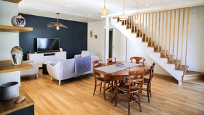 Un salon moderne doté d’un téléviseur à écran plat, d’une table à manger avec des chaises, d’un escalier et d’un mur d’accent de couleur sombre.