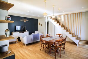Ein modernes Wohnzimmer mit Flachbildfernseher, Esstisch mit Stühlen, einer Treppe und einer dunkel gefärbten Akzentwand.