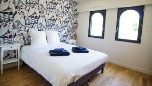 Une chambre à coucher avec un grand lit, deux tables de chevet, une commode et une fenêtre donnant sur un beau paysage.