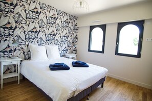 Ein Schlafzimmer mit einem großen Bett, zwei Nachttischen, einem Beistelltisch und einem Fenster mit Blick.