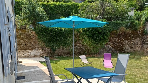 Een terras buiten met een tafel, stoelen, een blauwe parasol en een stenen muur op de achtergrond.