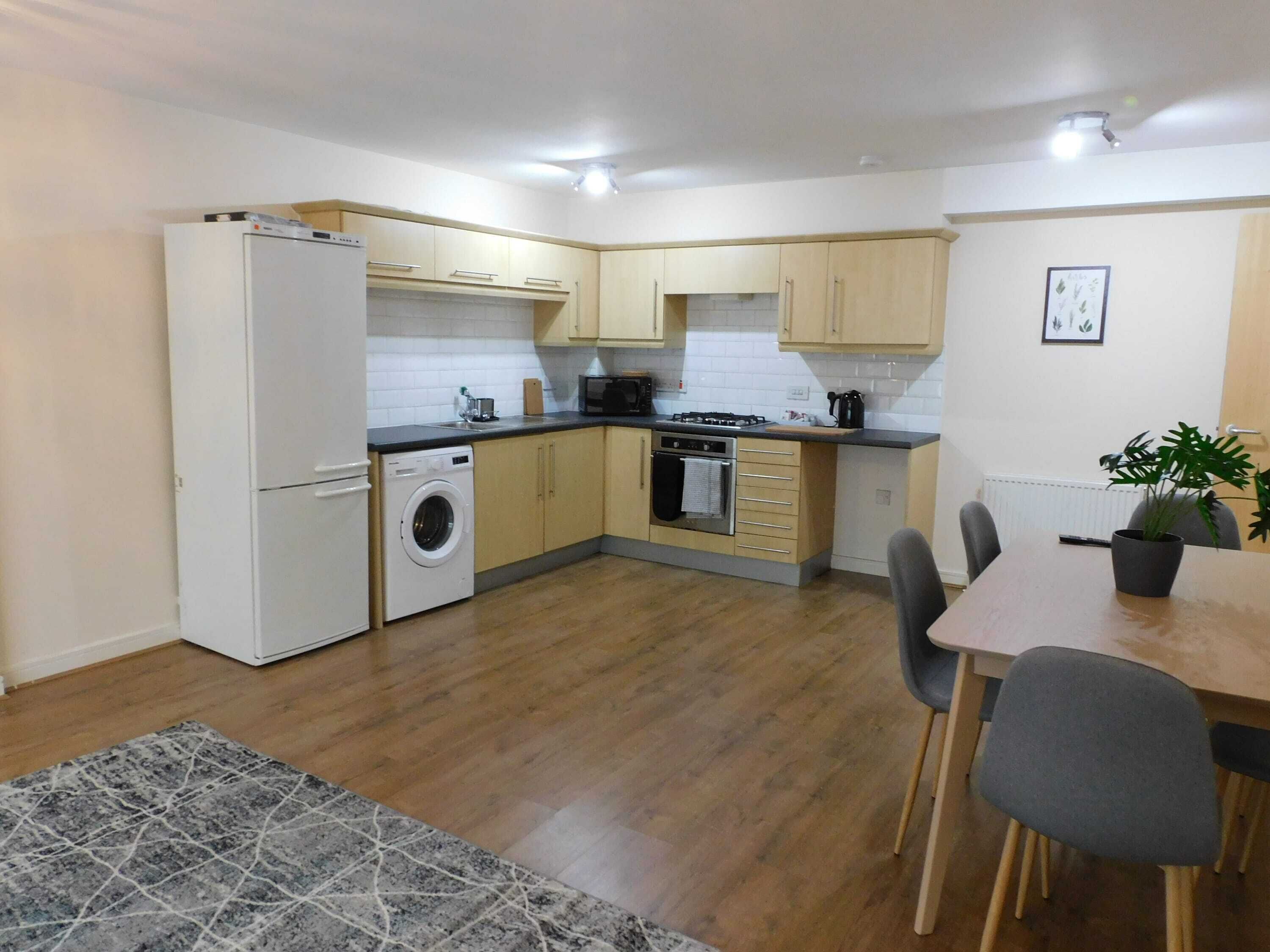 A compact kitchen with a washing machine, a stove, and a dining area with chairs.