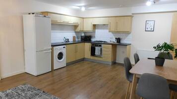 A compact kitchen with a washing machine, a stove, and a dining area with chairs.