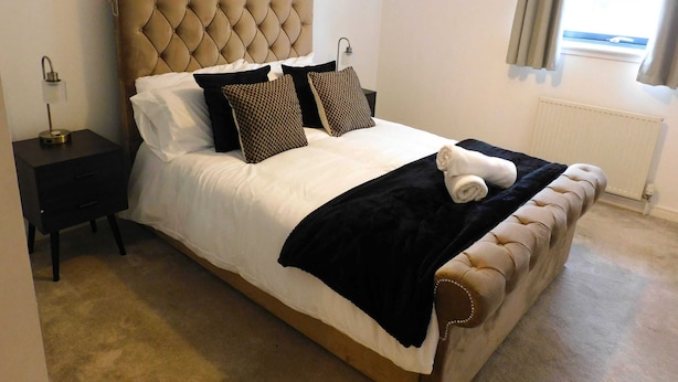 A neatly made bed with a tufted headboard, a bedside table with a lamp, and a window with curtains. - Fabulous, 2 bed apt, 10 mins from City Centre (Glasgow)