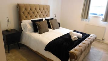 A neatly made bed with a tufted headboard, a bedside table with a lamp, and a window with curtains.